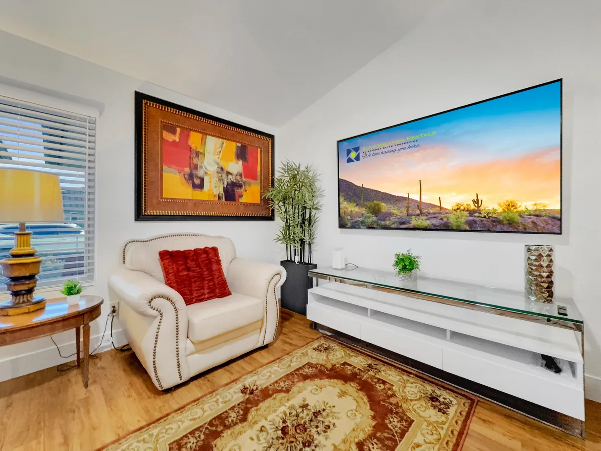 A cozy living area featuring a comfortable armchair, a large wall-mounted TV, colorful artwork, a decorative plant, and a stylish side table. The setup invites relaxation and unwinding after a productive day, with soft lighting and tasteful decor contributing to an inviting atmosphere.