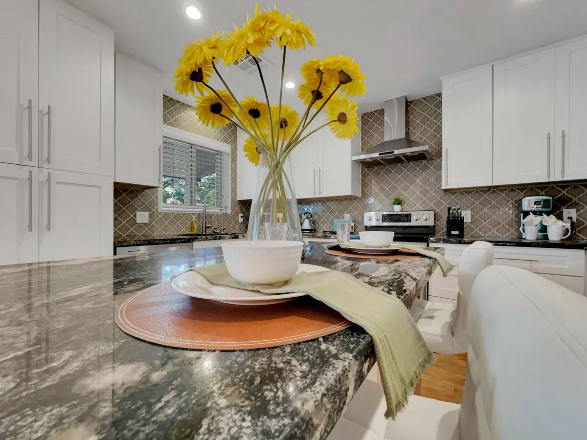 A close-up of a kitchen island with a granite countertop, set with plates and napkins, and adorned with a cheerful vase of yellow flowers. The setup suggests a space for sharing meals and casual gatherings.