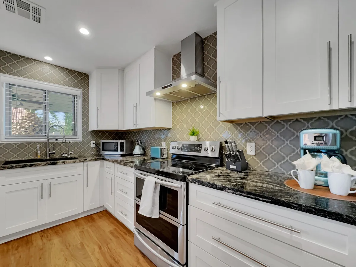 A stylish kitchen scene with prominent stainless steel appliances, a spacious granite countertop, a decorative backsplash, and various utensils and a coffee maker on display. The space feels both functional and welcoming, perfect for meal prep and entertaining.