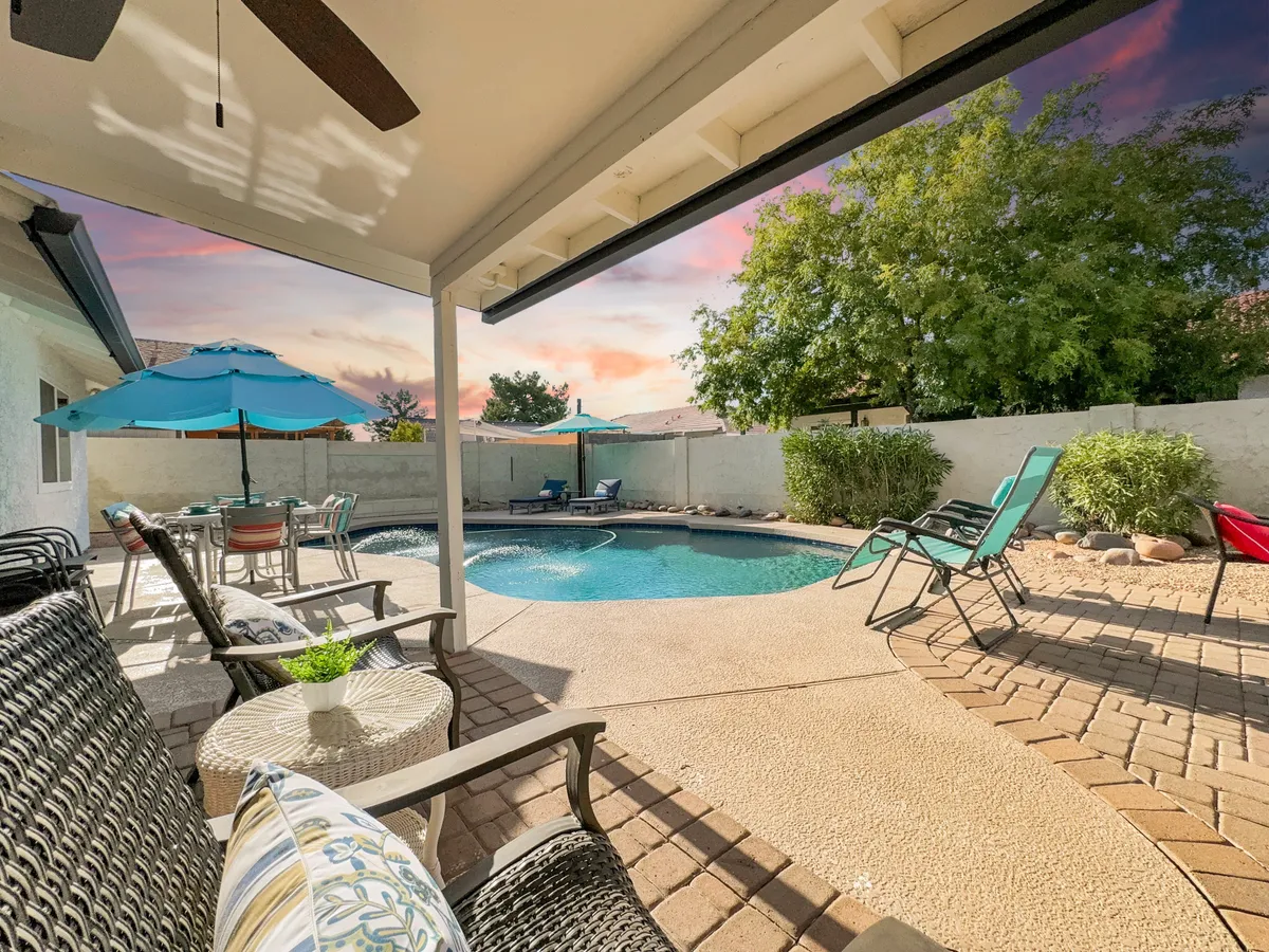 This image captures a sun-drenched backyard with a sparkling swimming pool, an inviting outdoor seating area shaded by an umbrella, and a beautifully landscaped garden. The setting is perfect for lounging, swimming, BBQs, or group gatherings under the open sky.