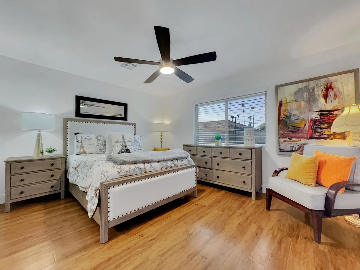 A serene bedroom featuring a neatly made bed with decorative pillows, artwork displayed above the headboard, matching nightstands with lamps, and soft, ambient lighting. The overall decor suggests a calming and restful atmosphere ideal for relaxation.