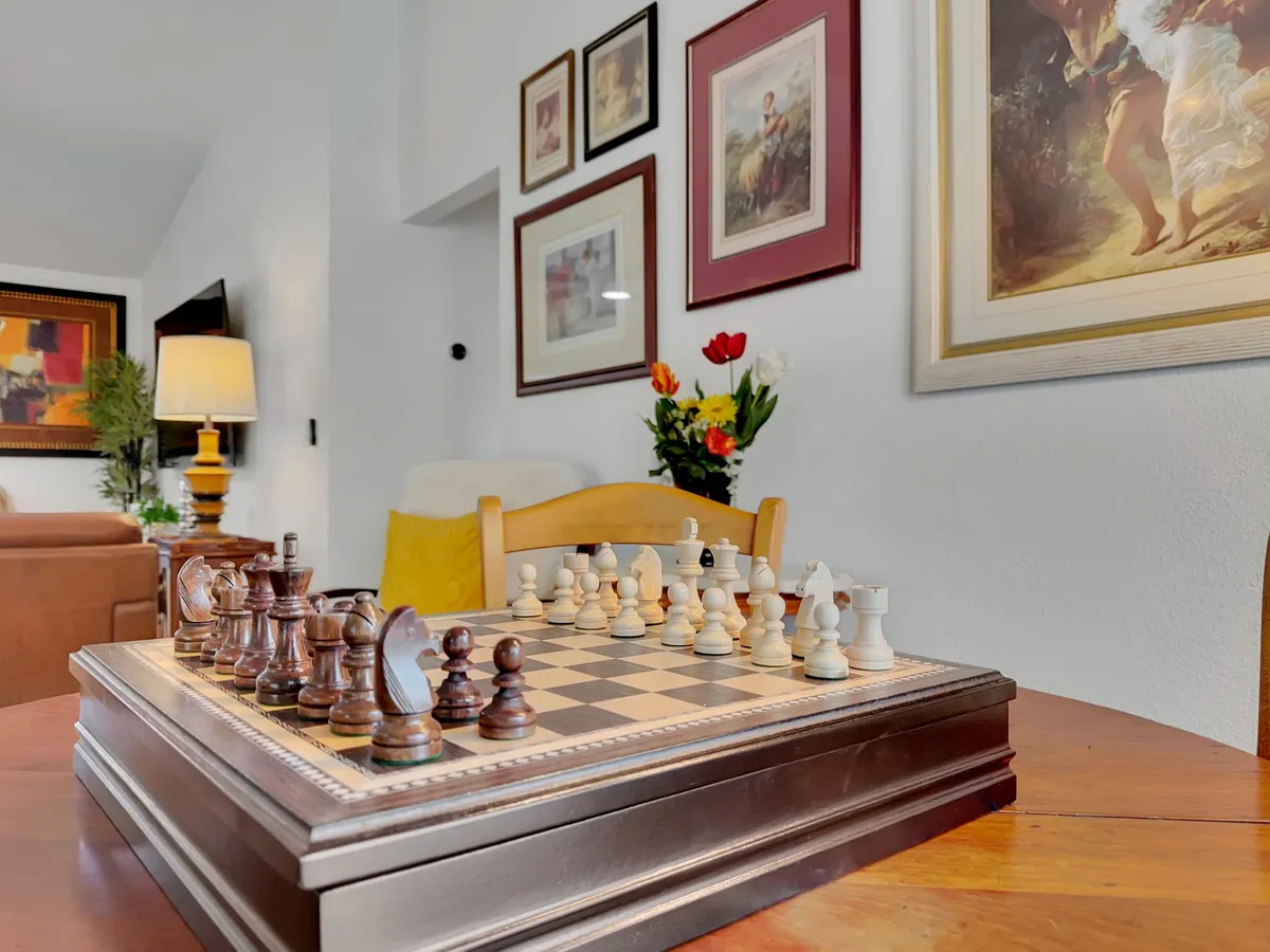 A thoughtfully designed corner with a chess set on the table, decorative paintings, tulip flowers, and a lamp. The vignette suggests a peaceful, intellectual spot for a break or casual strategizing, surrounded by art and a relaxing mood.