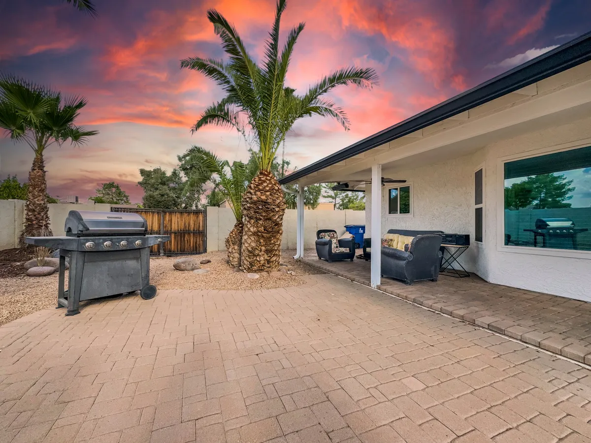 An inviting outdoor living space featuring a BBQ grill, comfortable sofa seating, palm trees, and a colorful evening sky. The setup is ideal for sunset dinners, twilight conversations, or relaxing with friends and family under the stars.