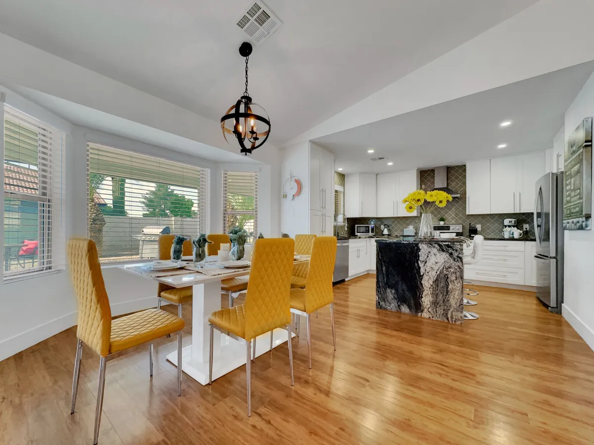A cheerful dining area with a bright dining table surrounded by yellow chairs, seamlessly connected to a modern kitchen. The kitchen island in the background suggests ease of movement and socializing between meal prep and dining.
