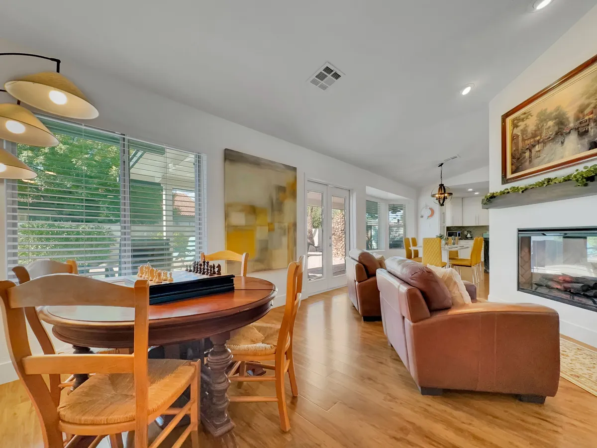A warmly lit living area featuring a dining table with a chess set, a comfortable sofa, and a fireplace beneath colorful artwork. The inviting arrangement encourages relaxation and intimate gatherings.