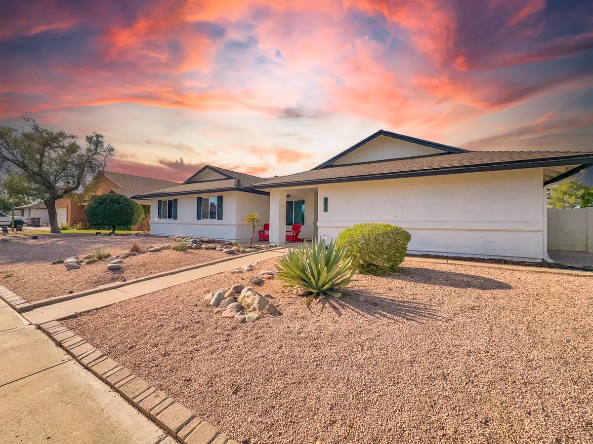 A serene front porch with vibrant red chairs overlooks a landscaped garden, all beneath a colorful sunset sky. This inviting entrance sets the tone for welcoming guests home from a day of local exploration.